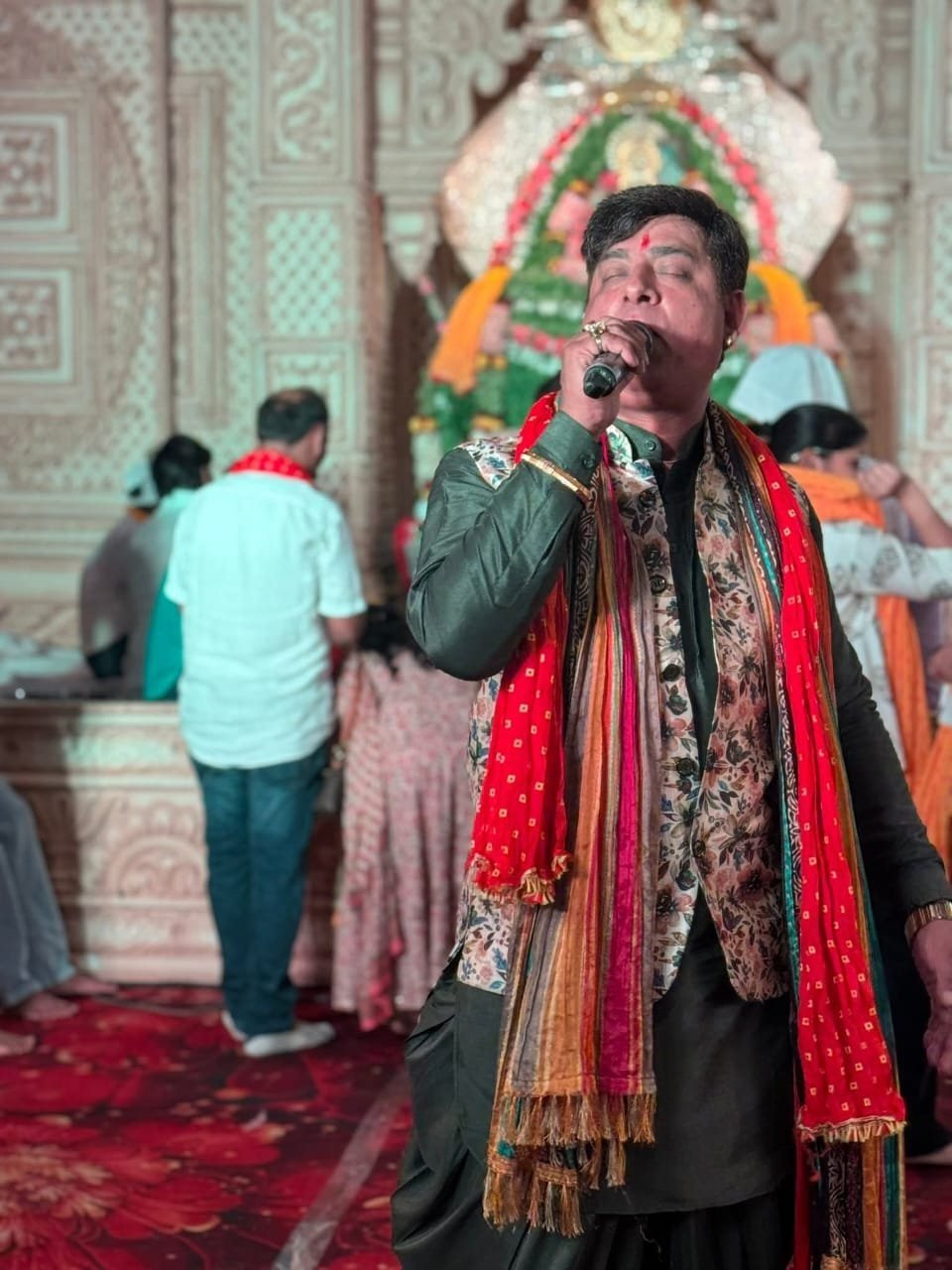 Devotional vocalist singing bhajans before a garlanded temple shrine during an evening programme