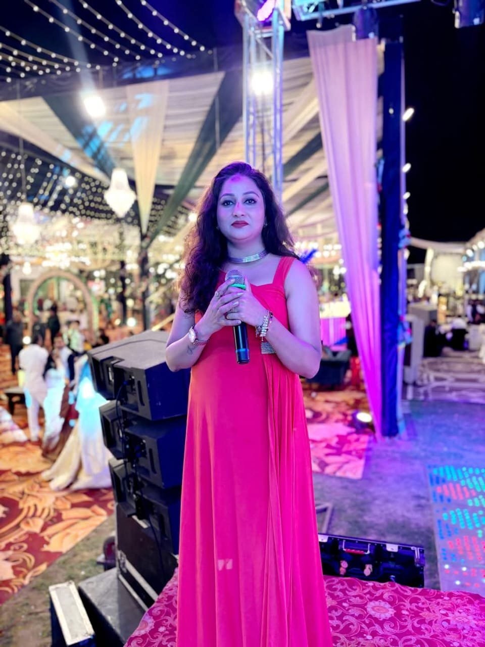 Female vocalist performing on an open-air wedding stage with festoon lighting and line-array speakers
