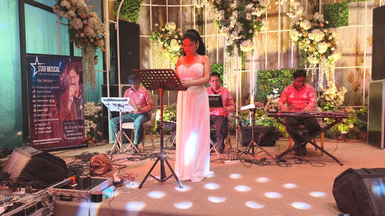 Female playback singer performing with keyboard and percussion musicians on a floral-decorated stage